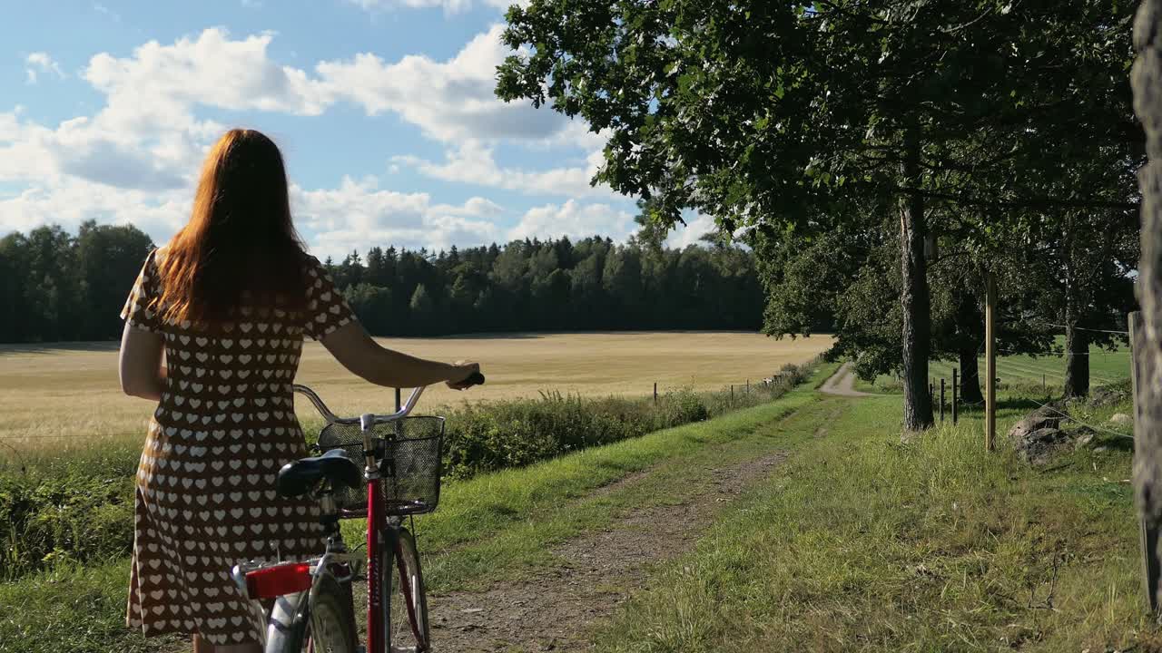 Mulher caminhando por uma estrada rural idílica com uma bicicleta.