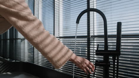 Woman in Bathrobe Adjusting Faucet in Modern Bathroom with City View