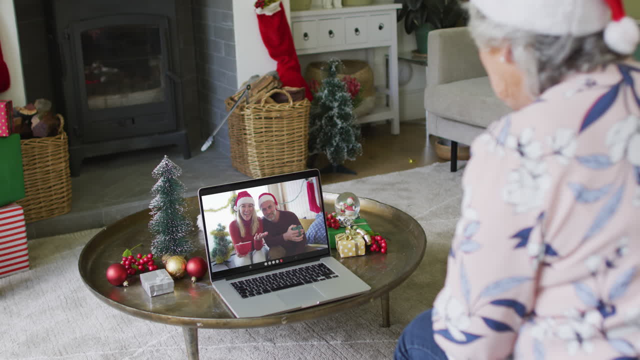 una mujer caucásica mayor agita y usa una computadora portátil para una llamada de video de navidad con una pareja en la pantalla