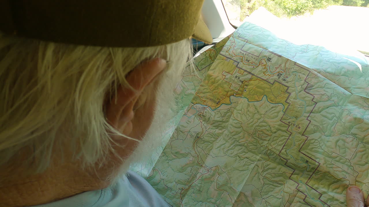 Old man preparing for hike, checking map sitting in his car