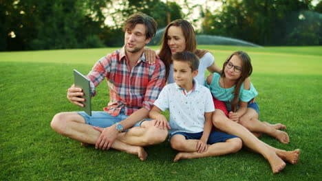 Man-holding-digital-tablet-with-family-in-park.-Parents-and-children-using-pad