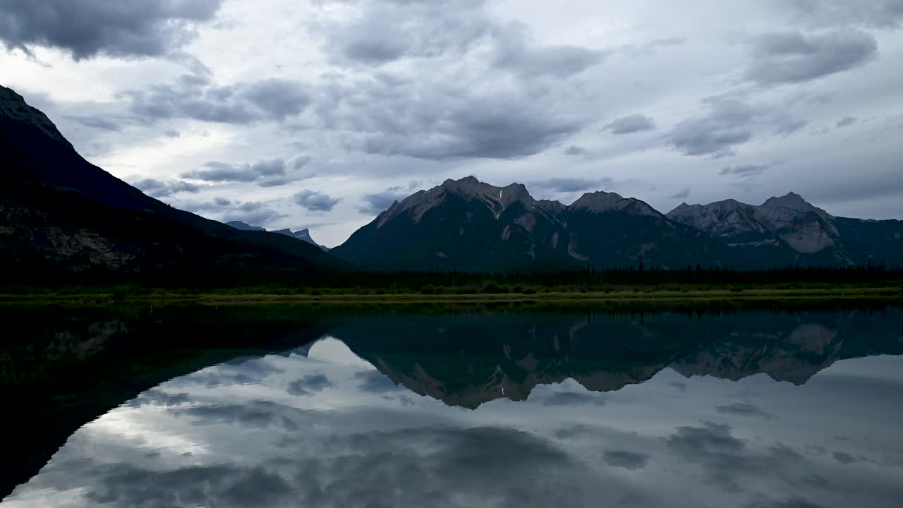 Calm mountain lake with small ripples in the evening. The mountains and clouds are perfectly reflected in the water.