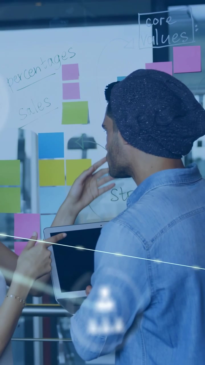 Vertical video: Duo with tablet placing notes on glass and pointing planning tech net sweeping team