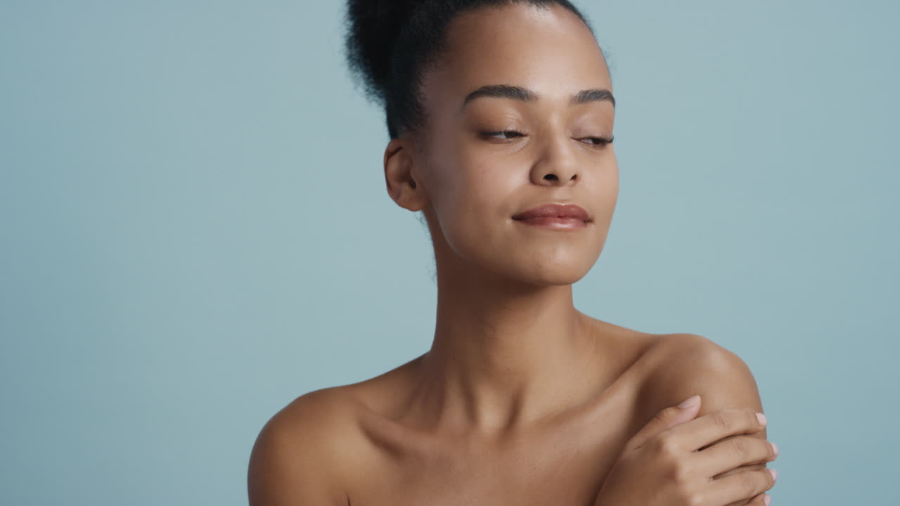 retrato de una hermosa mujer afroamericana tocando el cuerpo con la mano acariciando una piel suave y saludable disfrutando de una belleza natural perfecta con una apariencia confiada sobre un fondo azul concepto de cuidado de la piel