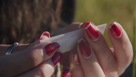 woman's hands with red nail polish rolling a piece of cigarette - close up