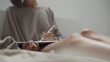 woman drawing on tablet in bed