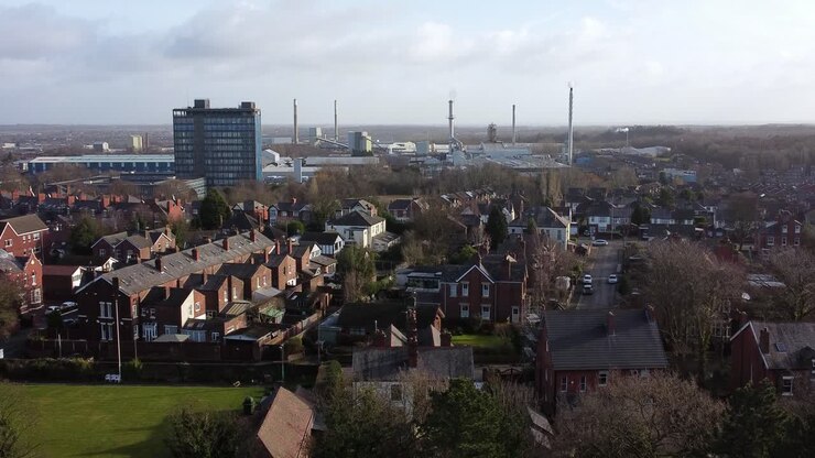 Vista aerea sopra gli alberi del parco verso il paesaggio urbano industriale e periferico con case e un grattacielo blu, Merseyside, Inghilterra