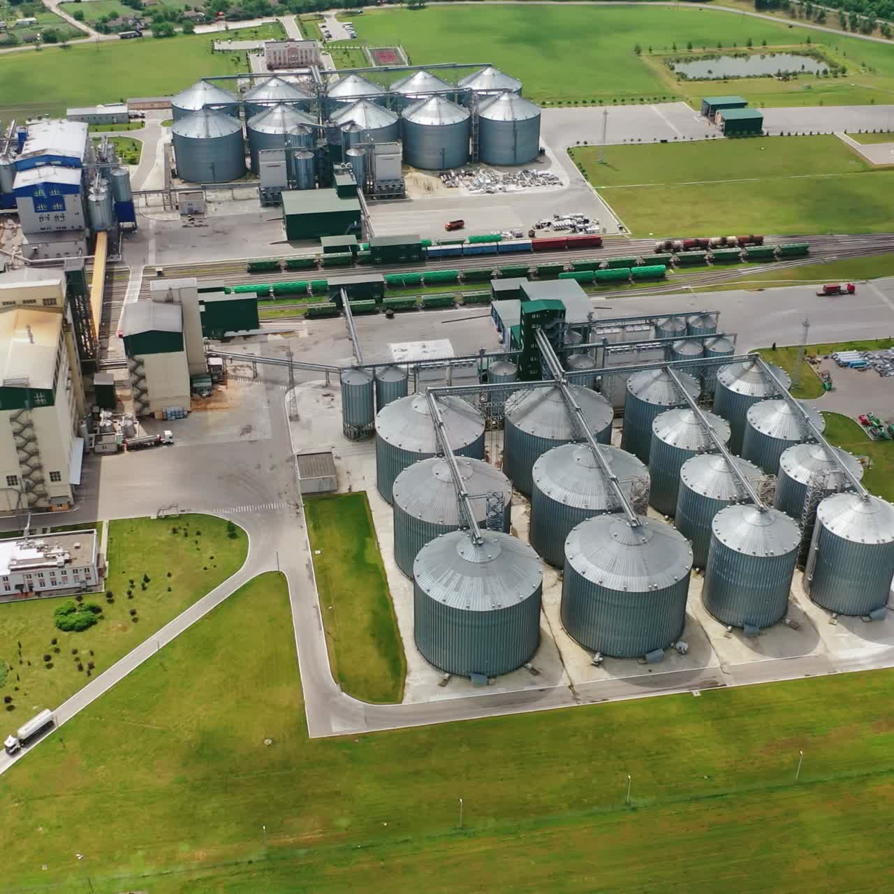 Large granary in field. A new built-in industrial grain elevator among nature. Silver containers for storing agricultural products. Aerial view.
