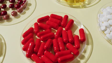 video close up of a variety of pills and capsules in glass dishes on yellow background