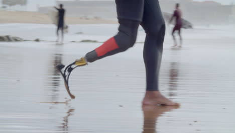 close up of an unrecognizable surfer in wetsuit with bionic leg running into the sea