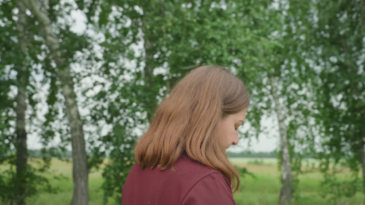 흰색 옷을 입은 여성이 자작나무 근처 땅을 조사하며 식물 채집가가 식물과 열매를 살피는 모습, 뒷모습과 옆모습, 몸을 굽혀 식물을 관찰하는 모습, 사려 깊은 시골 풍경, 은은한 여름 햇살, 식물학 애호가의 분위기