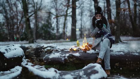 Woman-enjoying-and-drinking-her-tea-in-a-tree-branch-at-the-park-while-is-falling-snow