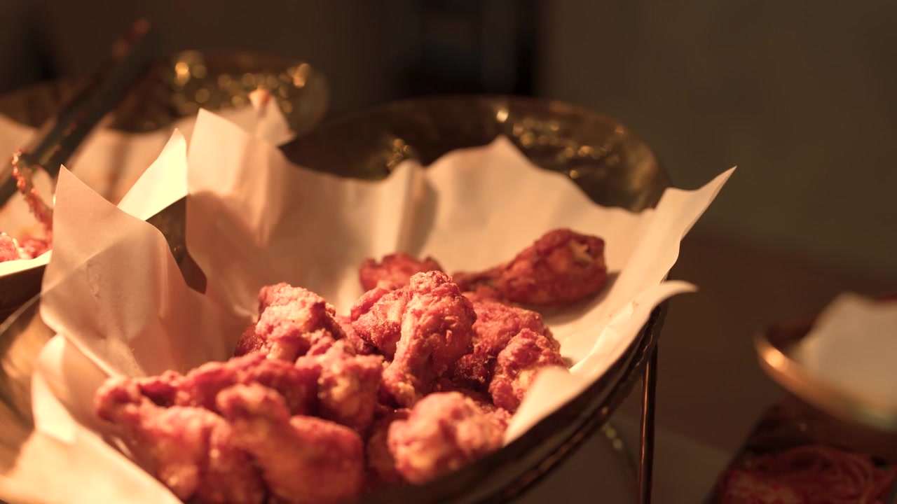 Primo piano di pinze metalliche che prendono pollo fritto croccante da un vassoio da buffet rivestito di carta