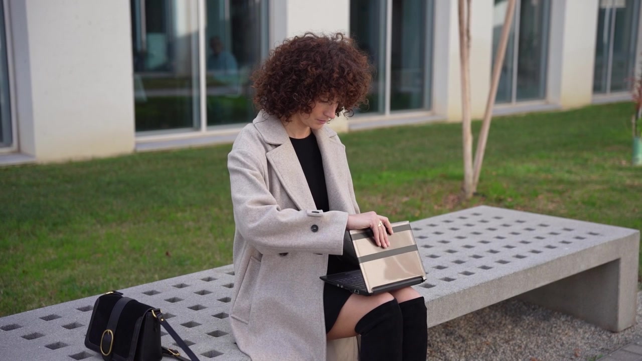 Una donna elegante vestita con un cappotto alla moda è seduta comodamente su una panchina all'aperto in città.