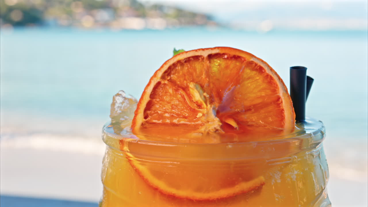 Primo piano di un cocktail arancione su un tavolo con una vista sfocata del mare sullo sfondo