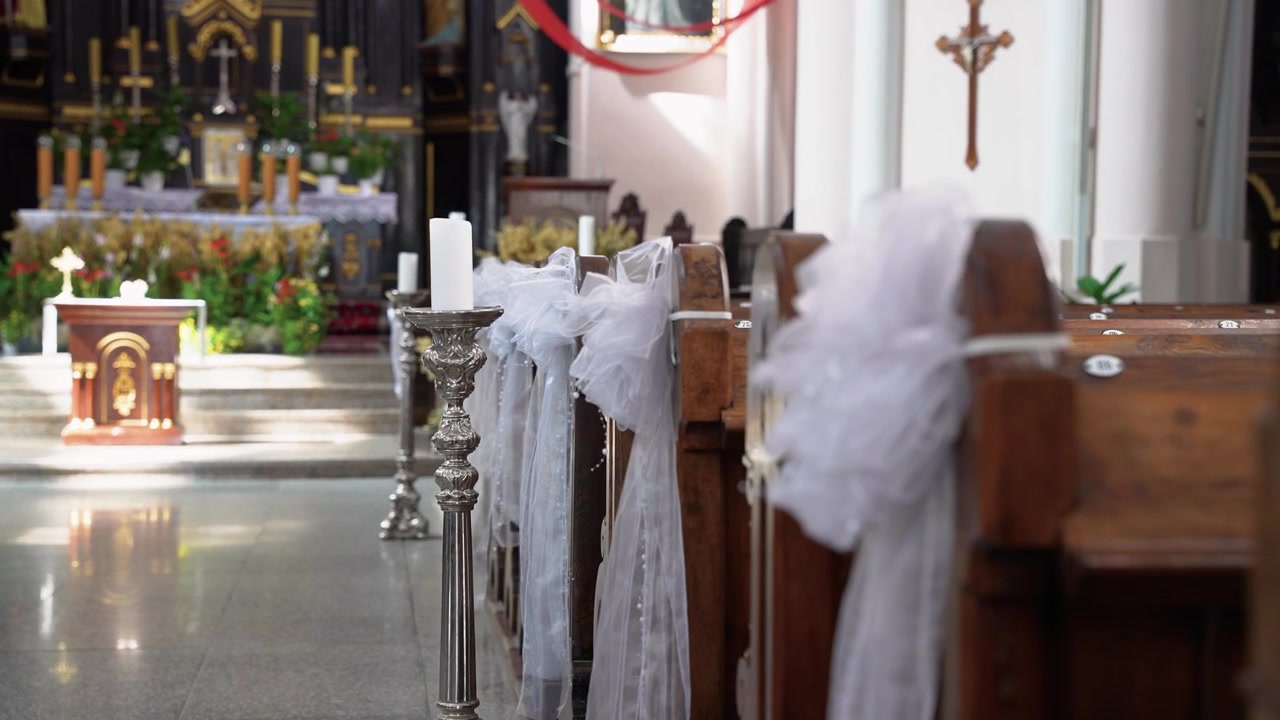 Navata della chiesa splendidamente decorata con nastri bianchi e candele, luce solare che filtra, altare ornato sullo sfondo. L'illuminazione naturale soffusa mette in risalto i banchi di legno lucidati. Nessuno presente