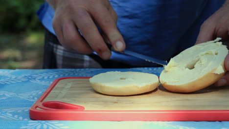 Nahaufnahme-Eines-Mannes,-Der-Bagel-Sandwich-Im-Freien-Auf-Einem-Picknicktisch-Beim-Camping-Macht