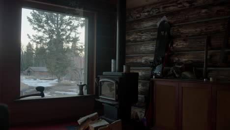 interior log cabin next to cold fireplace with a window view to a snowy farm