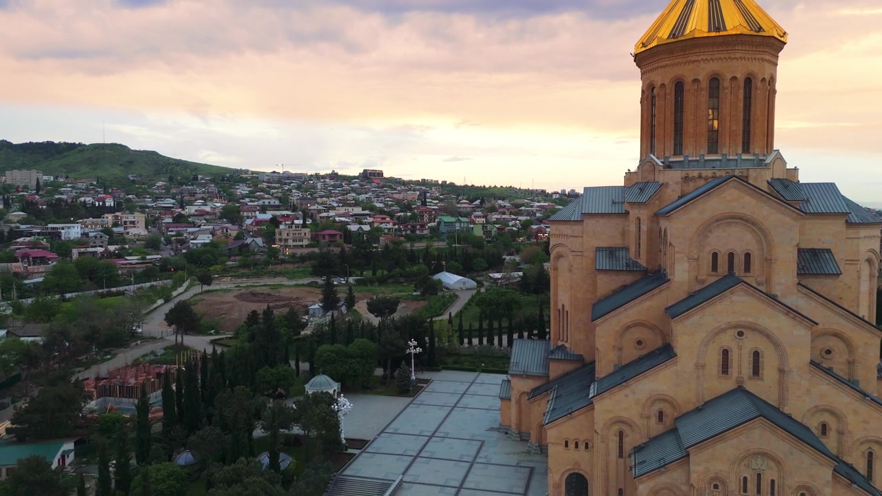 Luftfoto Dolly In: Solnedgang over Den hellige treenighetskatedralen Sameba og bybildet i Tbilisi, Georgia.