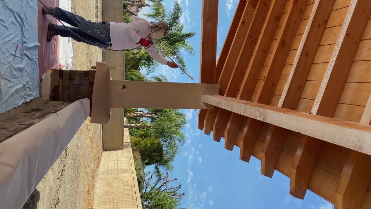 Professional painter coats wooden patio roof with primer using air gun, vertical