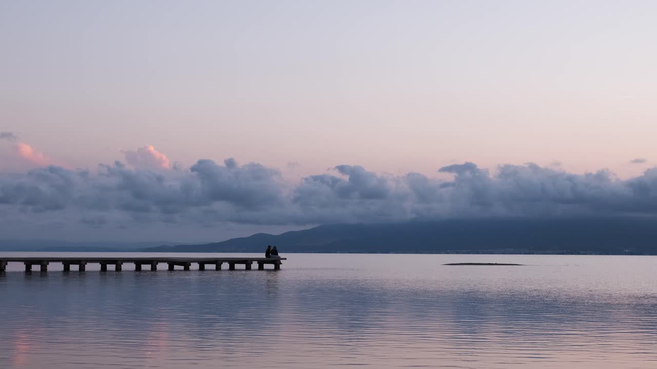 Unrecognizable persons relaxing on quay near sea in evening under sundown sky in summer
