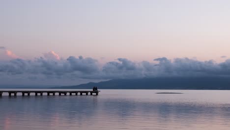 unrecognizable persons relaxing on quay near sea in evening under sundown sky in summer