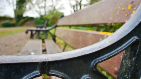 Low-view-close-shot-across-park-bench-iron-work-arms---bokeh-view-of-park-area