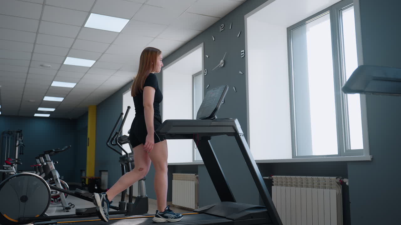 freelancer in casual gym outfit works out on treadmill adjusting speed and incline under bright natural light in modern fitness studio with exercise bikes and elliptical trainer visible behind