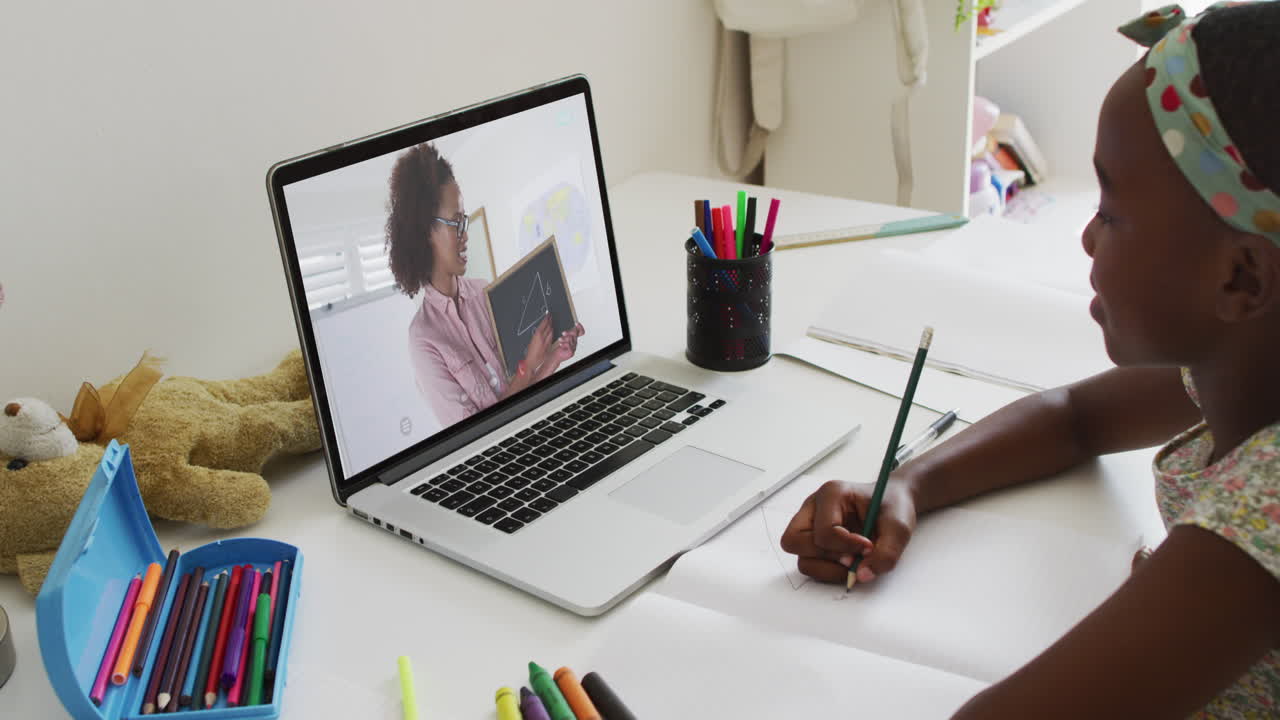 African american girl doing homework while having a video call with female teacher on laptop at home