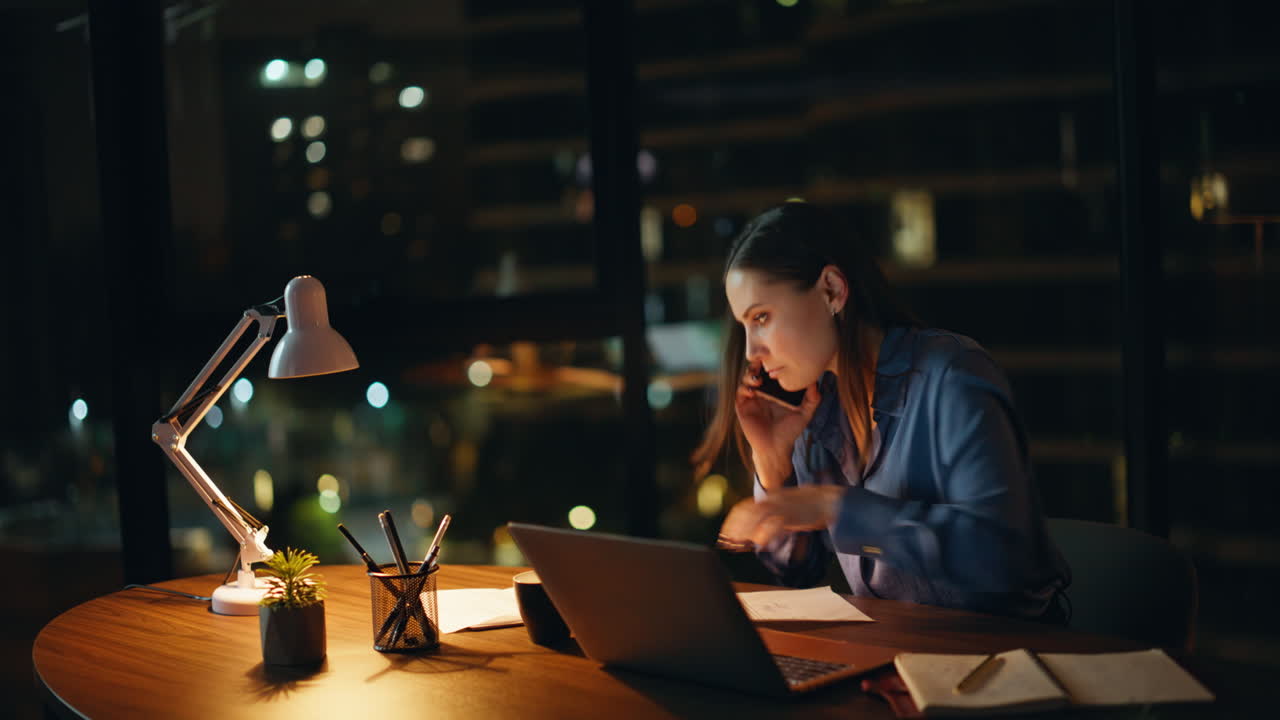 Overloaded executive talking cellphone checking papers at dark office desk