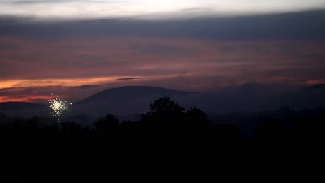 fireworks explode and burst into sparkling light as smoke rises against red sky in slow motion