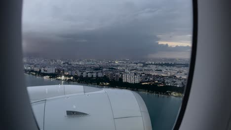 from the airplane window, witnessing city buildings along the singapore coastline illuminated by lightning amidst dark clouds - pov