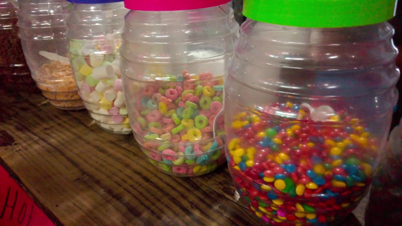 Colorful candy and sweet treats displayed in clear plastic jars on a wooden market counter, showing assorted shapes, textures, and bright colors in Mexico