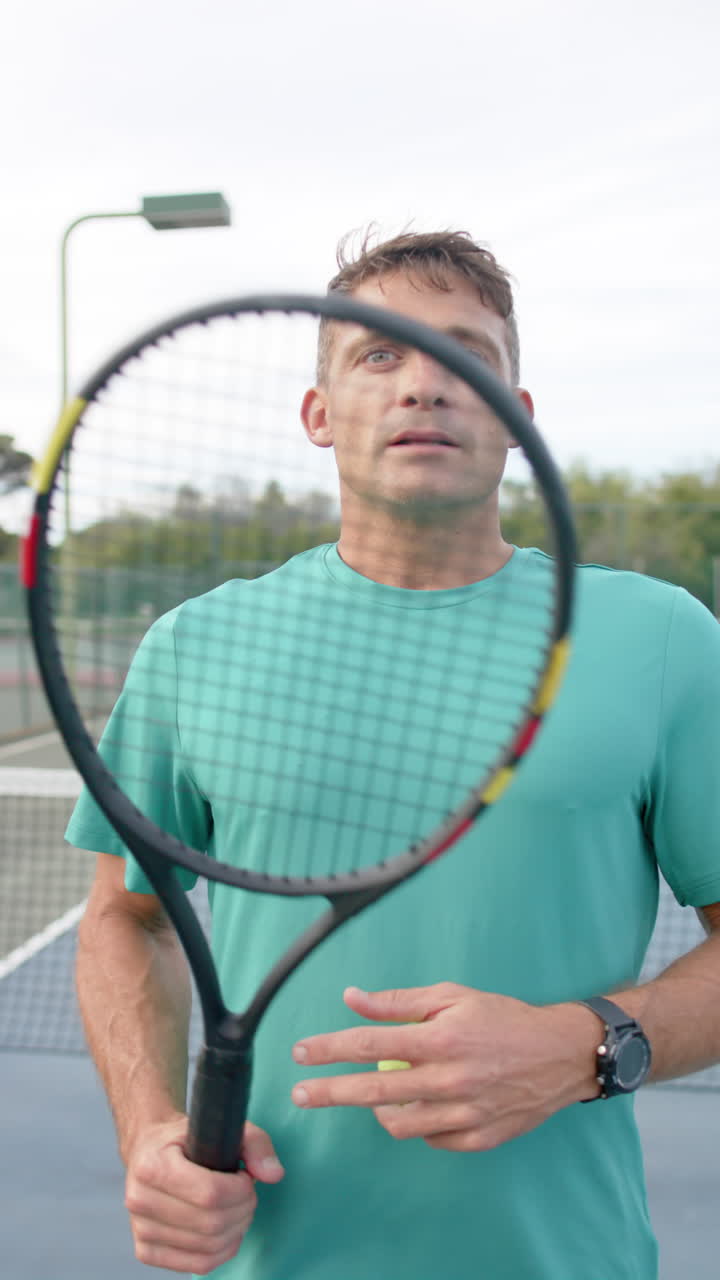 Vertical video of portrait of focused caucasian man with tennis racket in slow motion