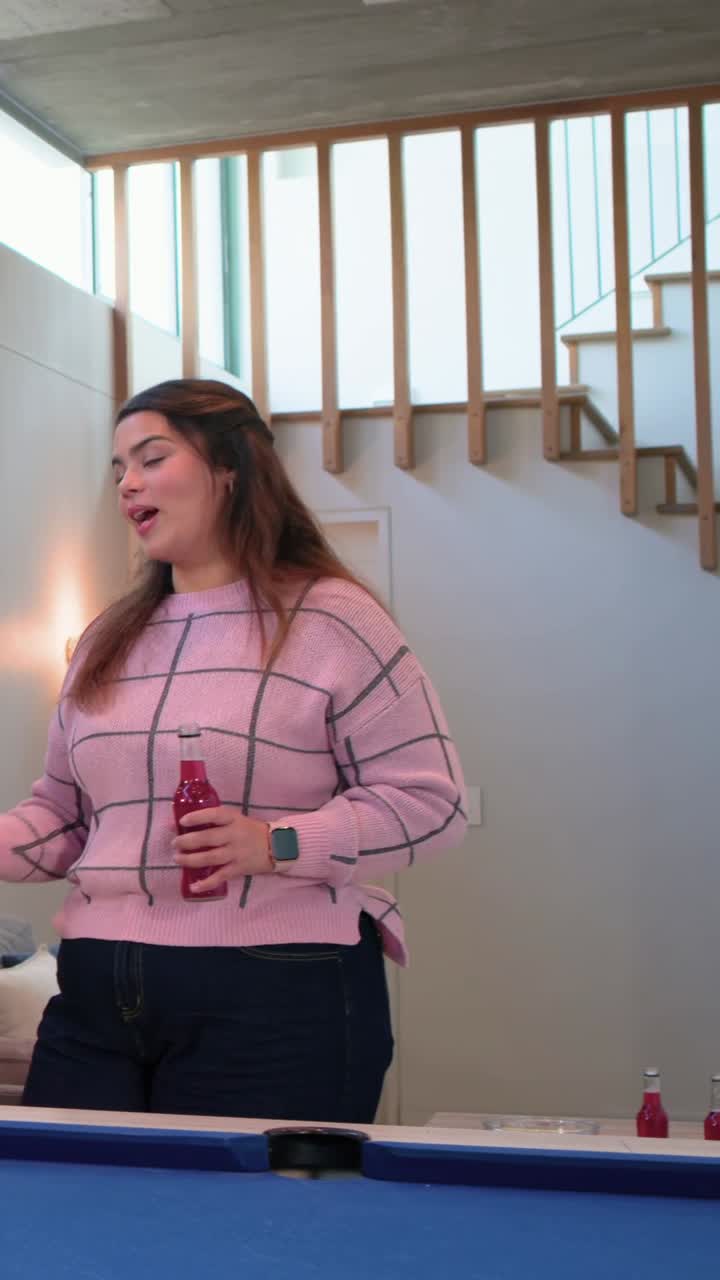 Video verticale: Donna in top rosa che entra, tiene una stecca e mette il gesso sulla stecca a un tavolo da biliardo blu di casa per giocare a biliardo.