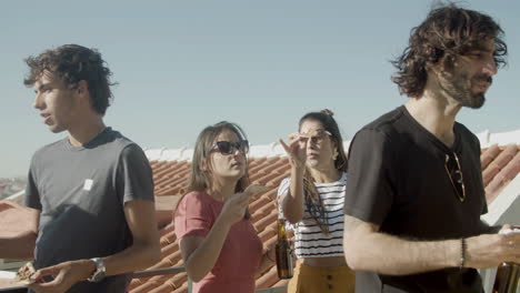 carefree friends talking together while eating pizza and drinking beer during a rooftop party