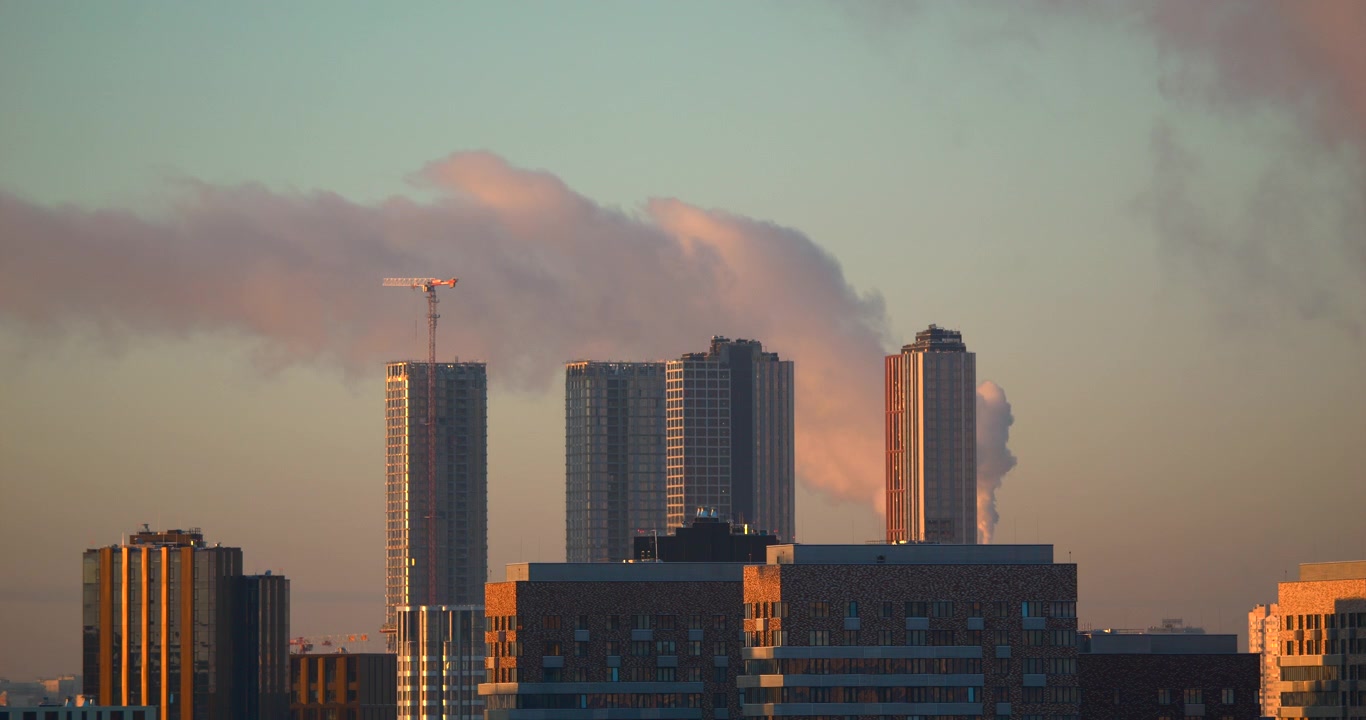 Nuvem de fumaça rosa ao entardecer flutua atrás de torres de cidade modernas e guindaste de construção para desenvolvimento urbano, indústria de poluição do ar e visuais atmosféricos do horizonte