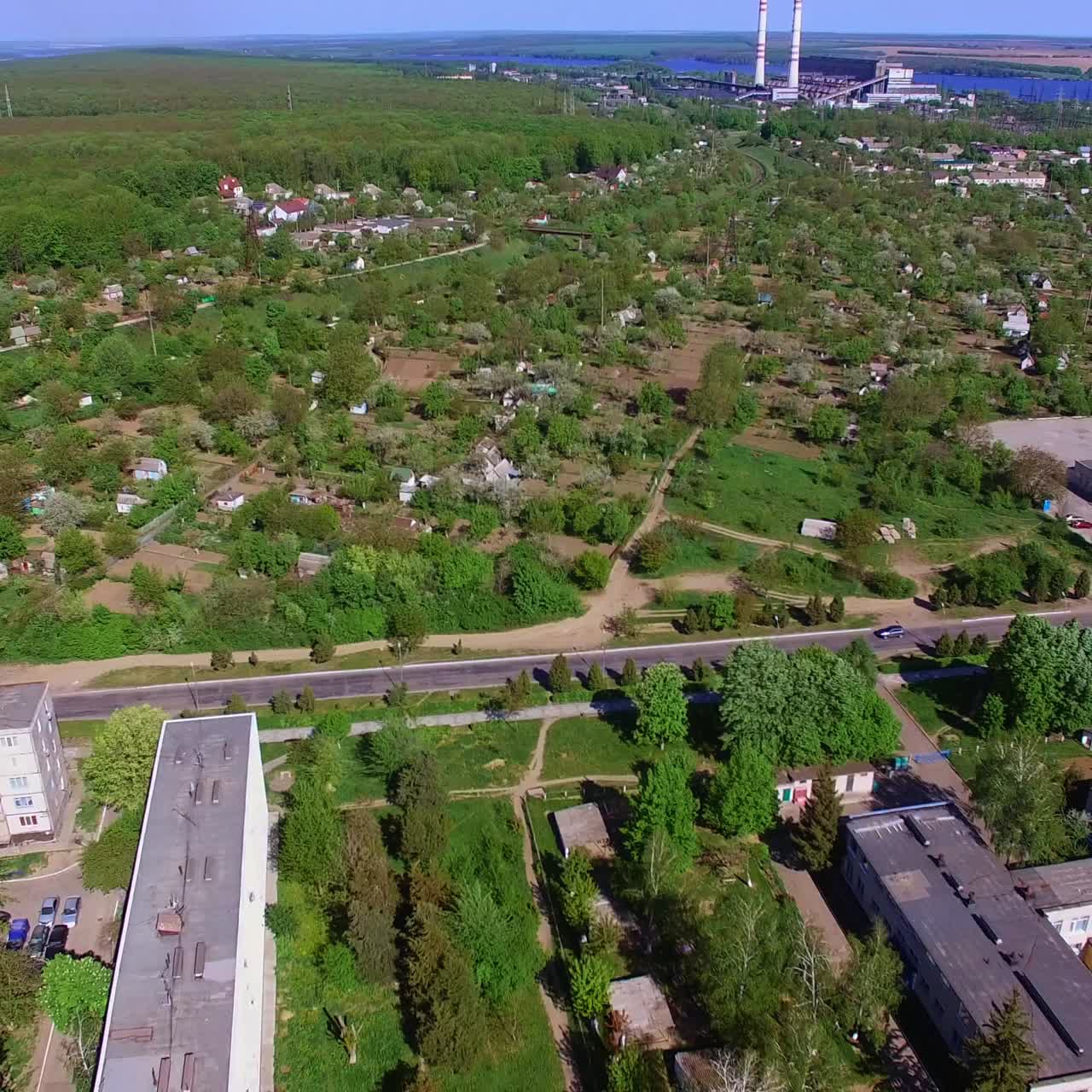 Green sunny city with lots of blocks of flats and cottages. Beautiful river at backdrop separating the city from farmlands