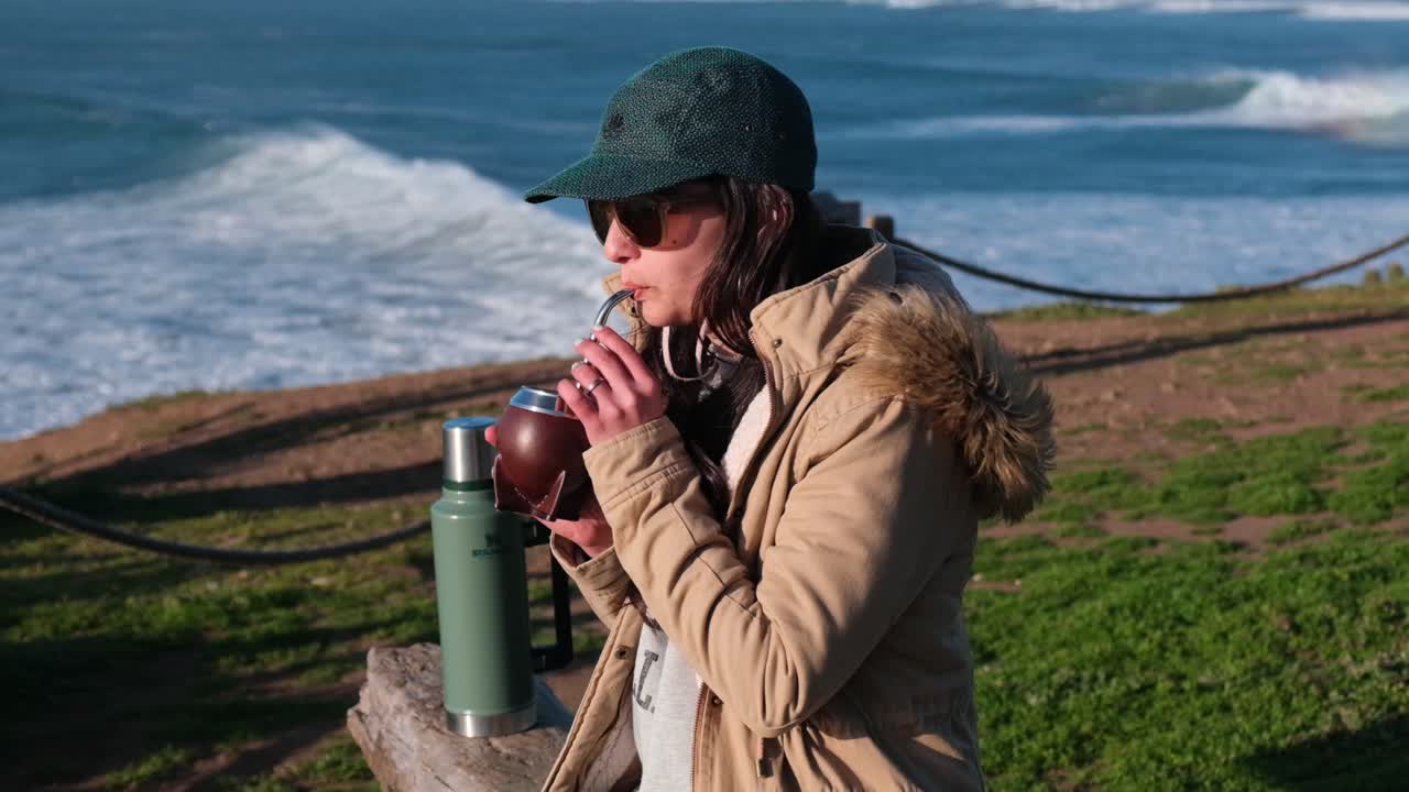 mujer bebiendo mate, bebida típica argentina, en la playa, mientras ve la puesta de sol pichilemu, punta de lobos, playa para surfear, chile