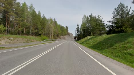 the car travels along the road and eventually drives under a stone bridge, continuing its journey through the scenic route