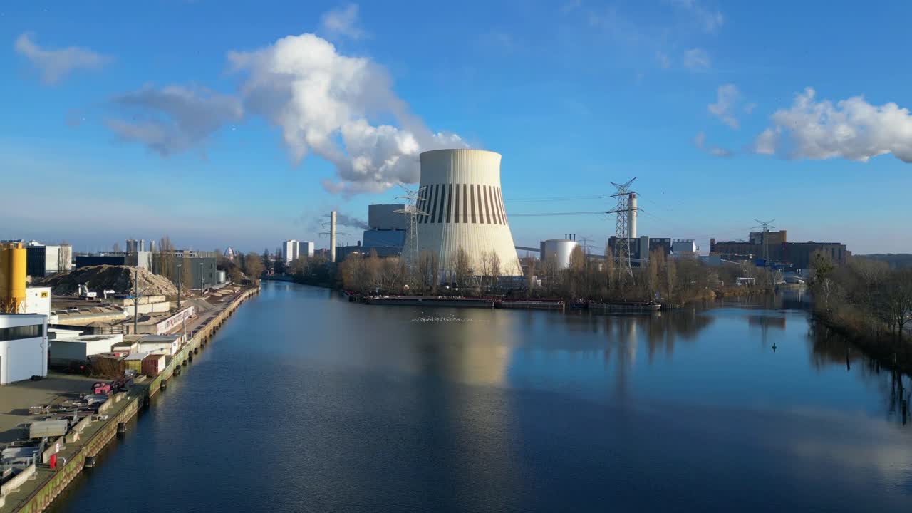 power plant emitting steam from its cooling tower, situated by a river and overlooking the cityscape. Perfect aerial view flight ascending drone