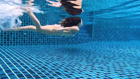 mujer nadando bajo el agua en una piscina de azulejos