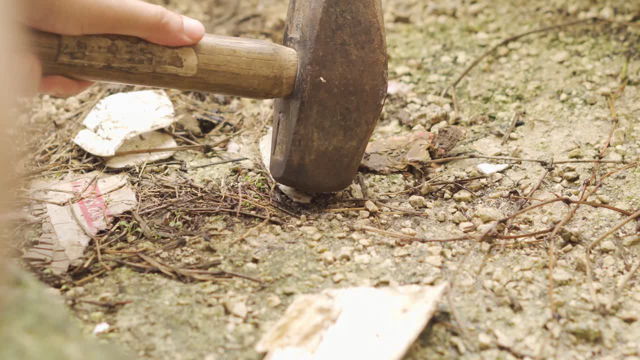 Hand Picks Up Hammer and Starts Breaking Through Ground