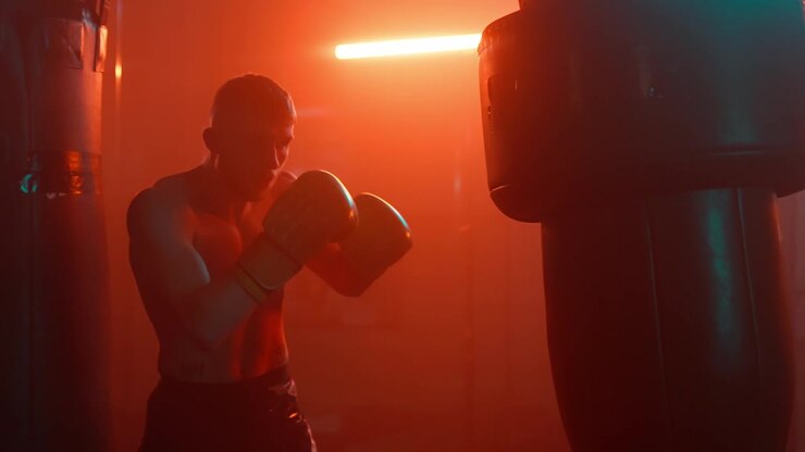 Hombre entrenando con un saco de boxeo en un gimnasio de boxeo iluminado en rojo