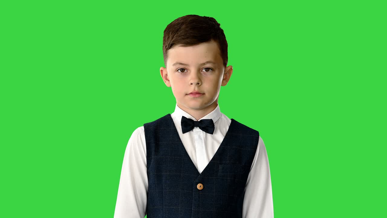 niño confiado en corbata de papagaio y chaleco cruzando los brazos mientras mira a la cámara en una pantalla verde, clave de croma