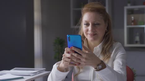 mature businesswoman working in home office looking at her phone.