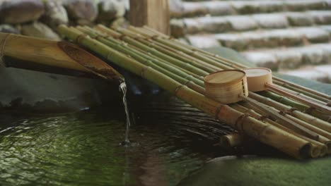 Wasser-Fließt-Aus-Einem-Bambusrohr-In-Einen-Brunnen-Mit-Zwei-Hölzernen-Schöpflöffeln,-Die-In-Der-Nähe-Am-Schrein-In-Shirakawago-Ruhen