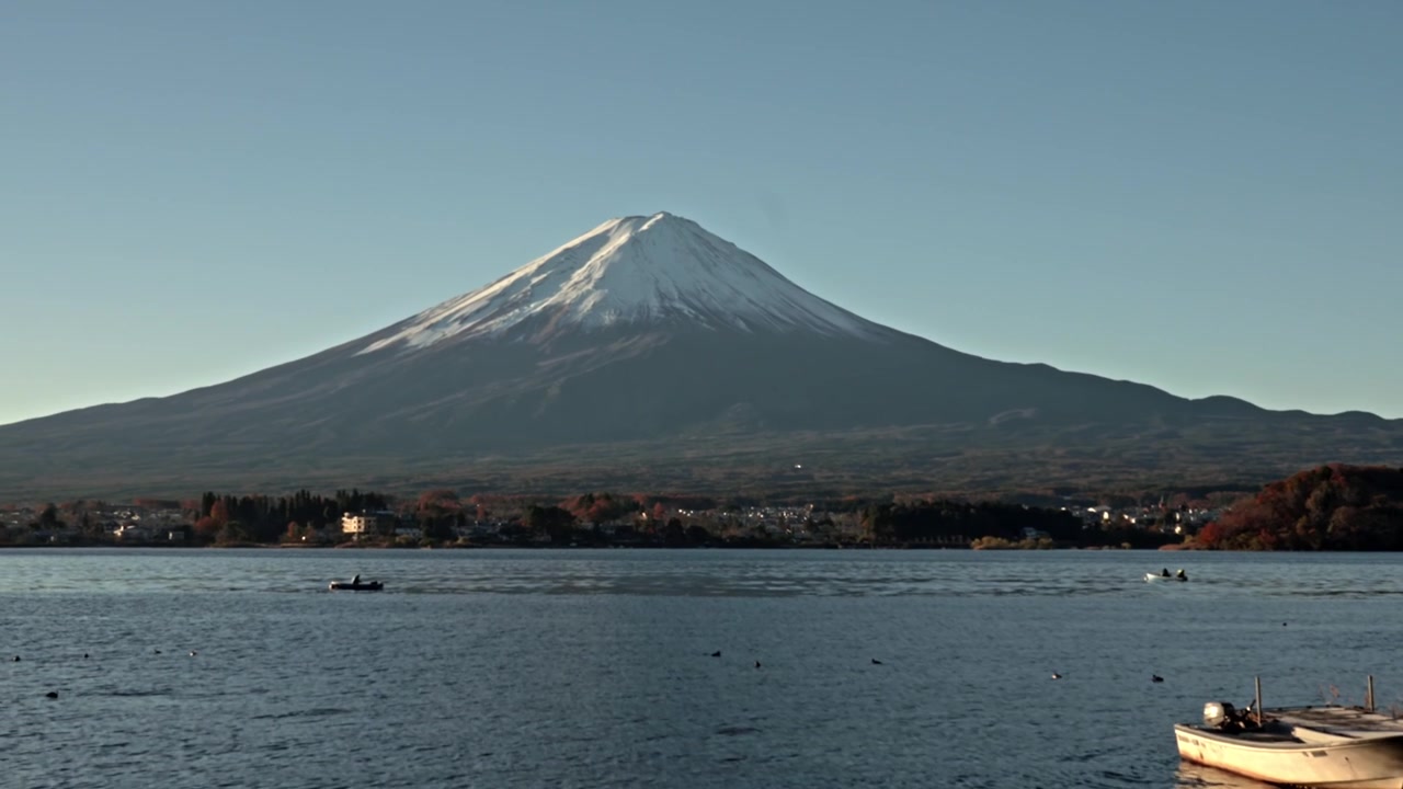 Una fluida inclinazione della telecamera verso l'alto, che parte da piccole barche sulla riva del Lago Kawaguchiko, si muove sull'acqua per rivelare il Monte Fuji e termina con vivaci foglie d'acero rosse autunnali che incorniciano la parte superiore.