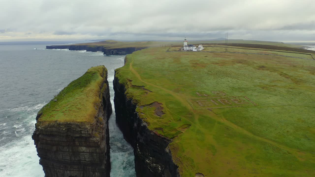 el tiro de establecimiento revela capas de acantilados dramáticos y pilas de mar en la cabeza del bucle, con el faro en el fondo