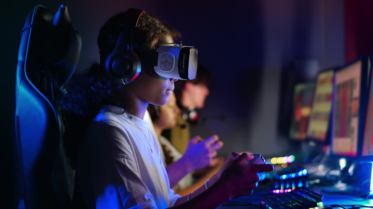 Black teen smiling girl in VR headset playing video games in video game club with blue illumination using a gamepad